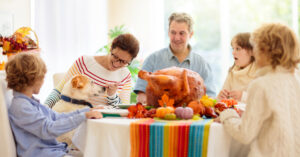 family gathered around Thanksgiving table offering dog a piece